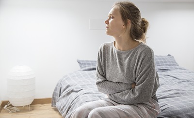 En kvinde med smerter i underlivet pga. Blødningsforstyrrelser sidder på en seng.
