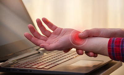 En person holder sig til sit håndled pga. seneskedebetændelse i håndleddet, hvor at der vises med rød, hvor smerten sidder.