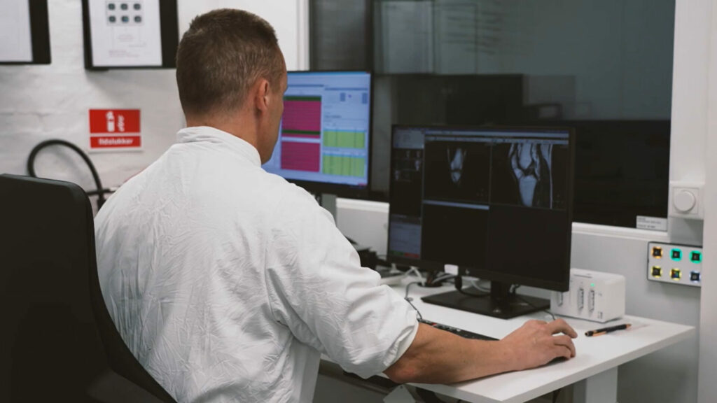 Radiograf sidder foran to skærme ved en mr scanner