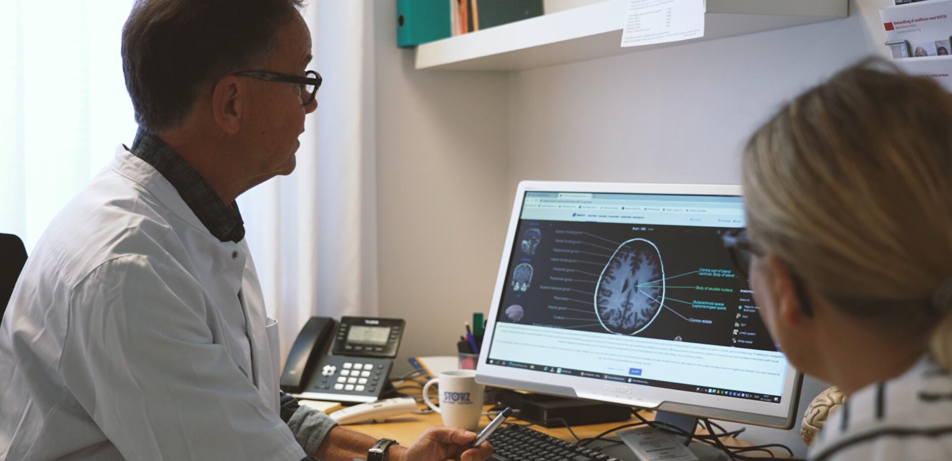 Neurolog ved skrivebord forklarer patient mr scanning af hjernen