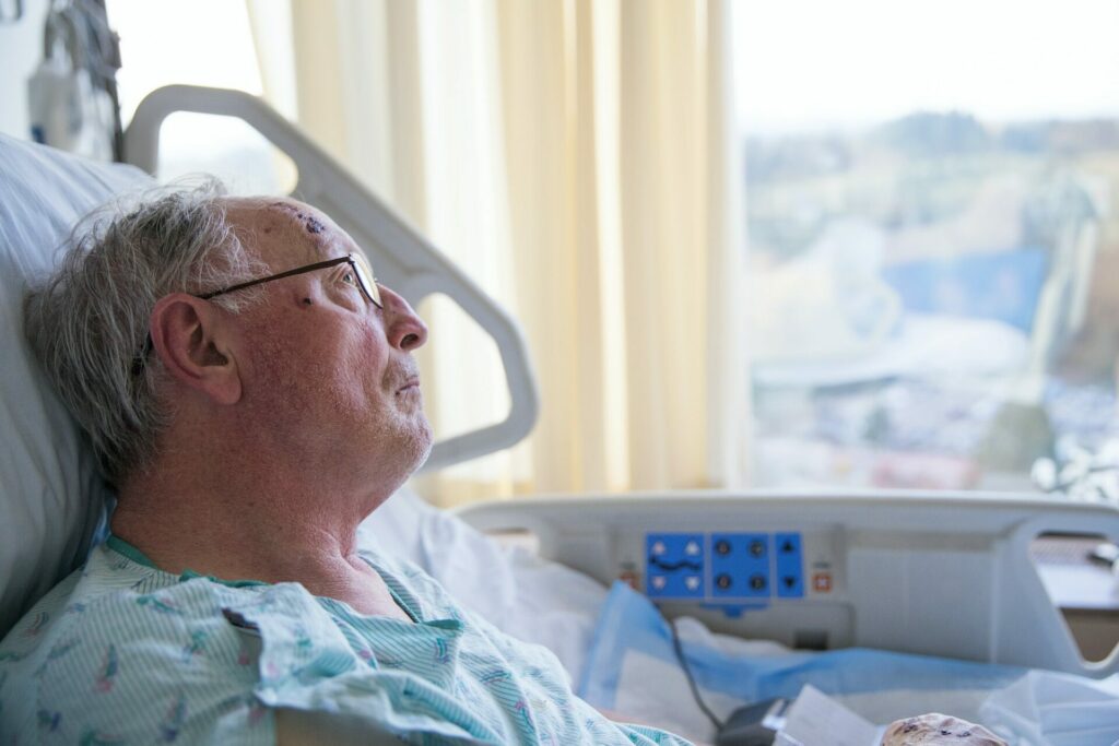Ældre mand i hospitalsseng kigger ud af vinduet
