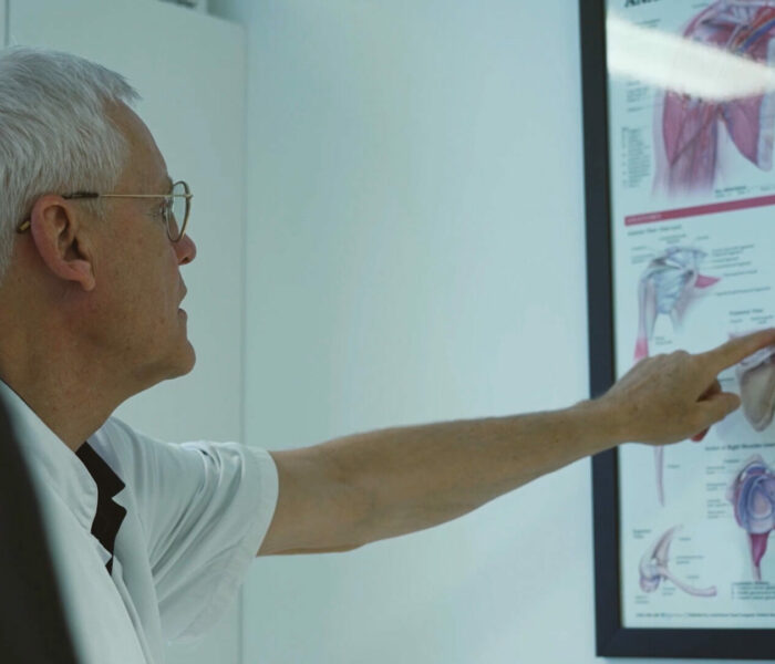 Ortopædkirurg peger forklarende på en plance med skulder tegninger